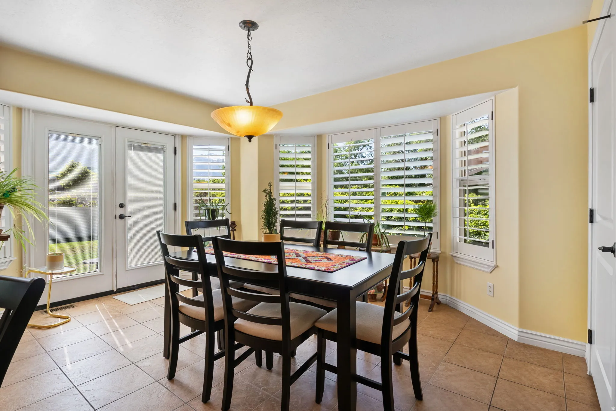 Dining area featuring tiled flooring, a bay window with plantation shutters, and a suspended ceiling light fixture