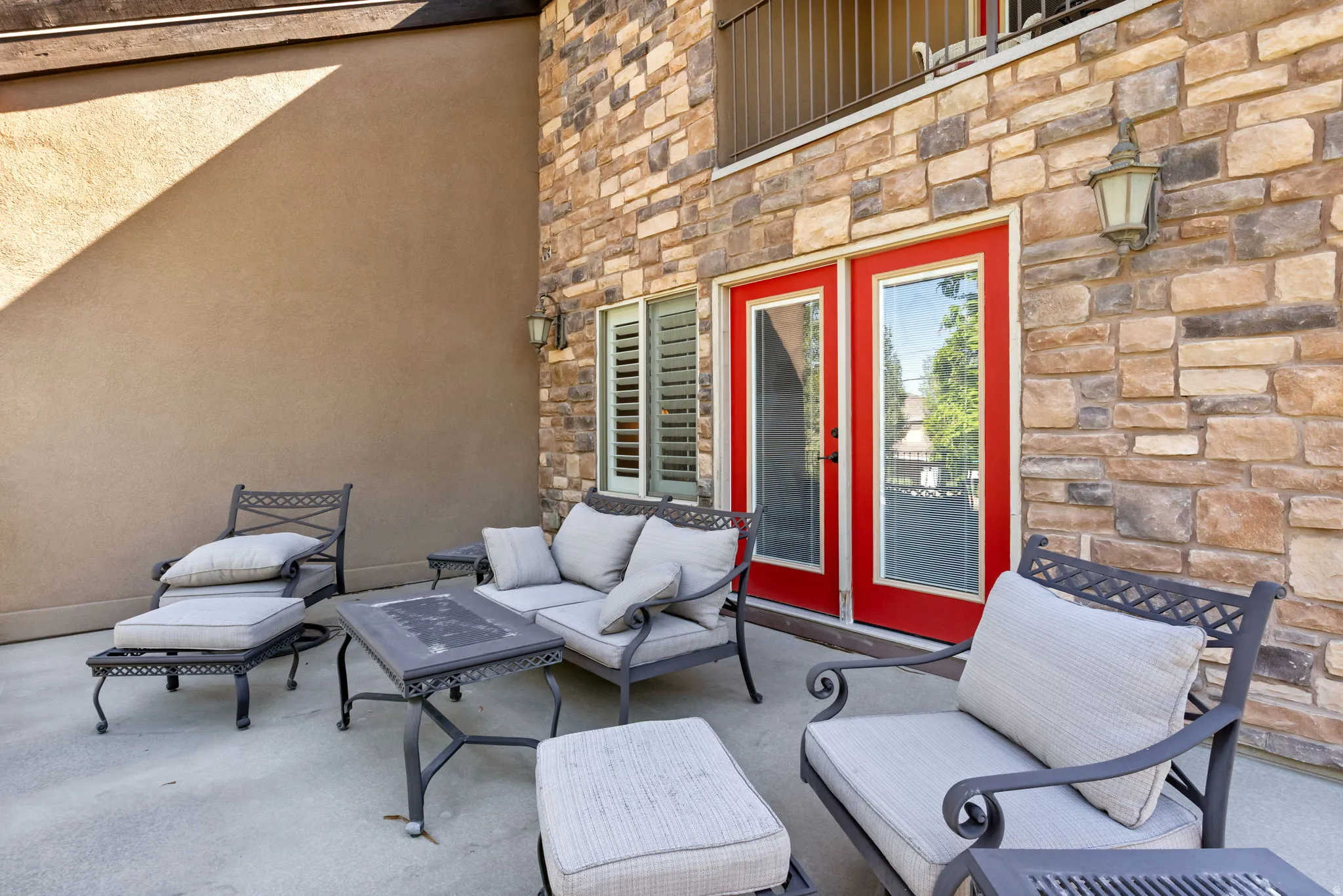 Outdoor patio featuring a stone veneer wall, stucco siding, and red-framed glass doors