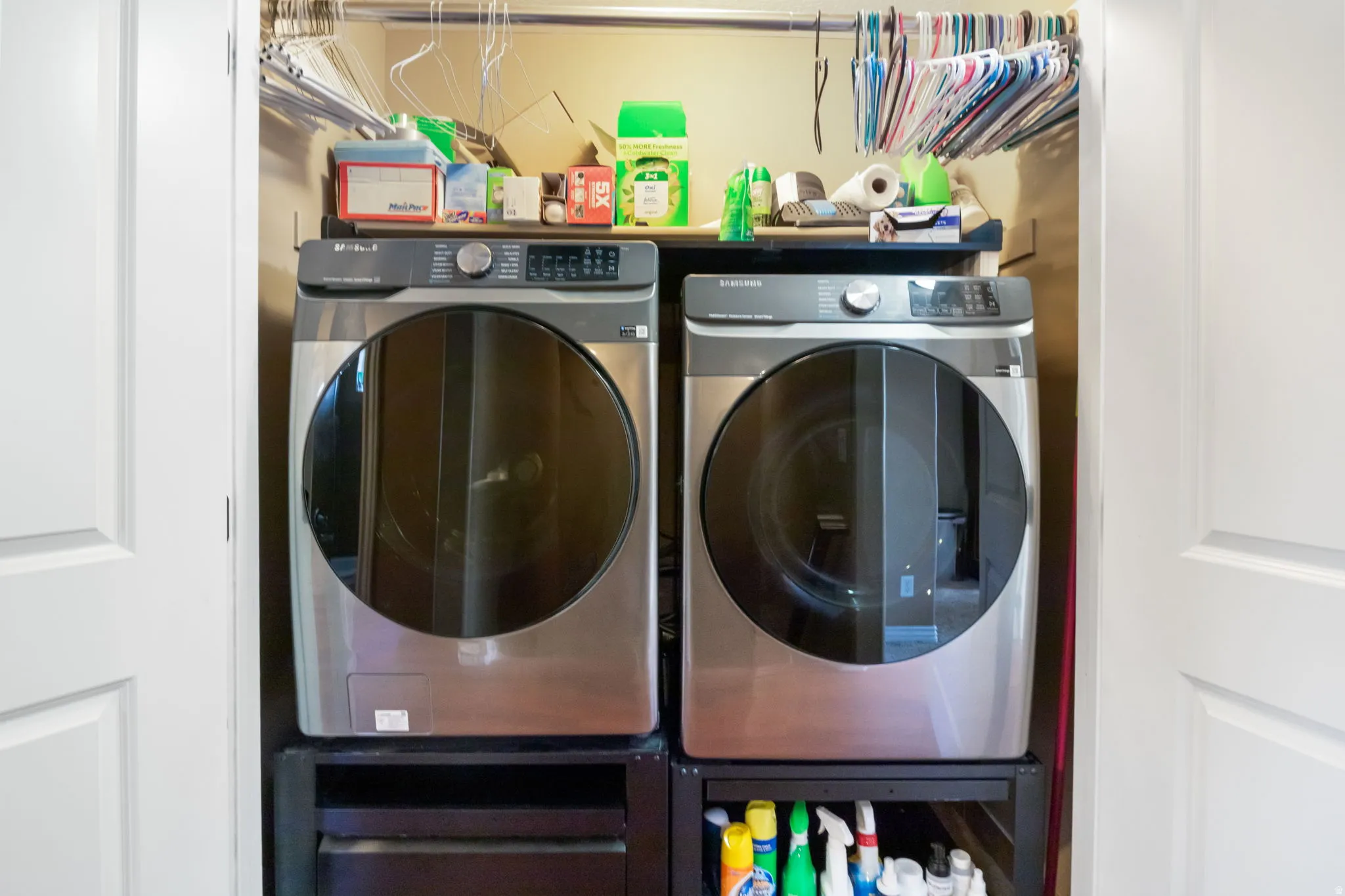 Dedicated laundry closet featuring a stainless steel front-load washer and dryer set, white bi-fold doors, and an upper storage shelf