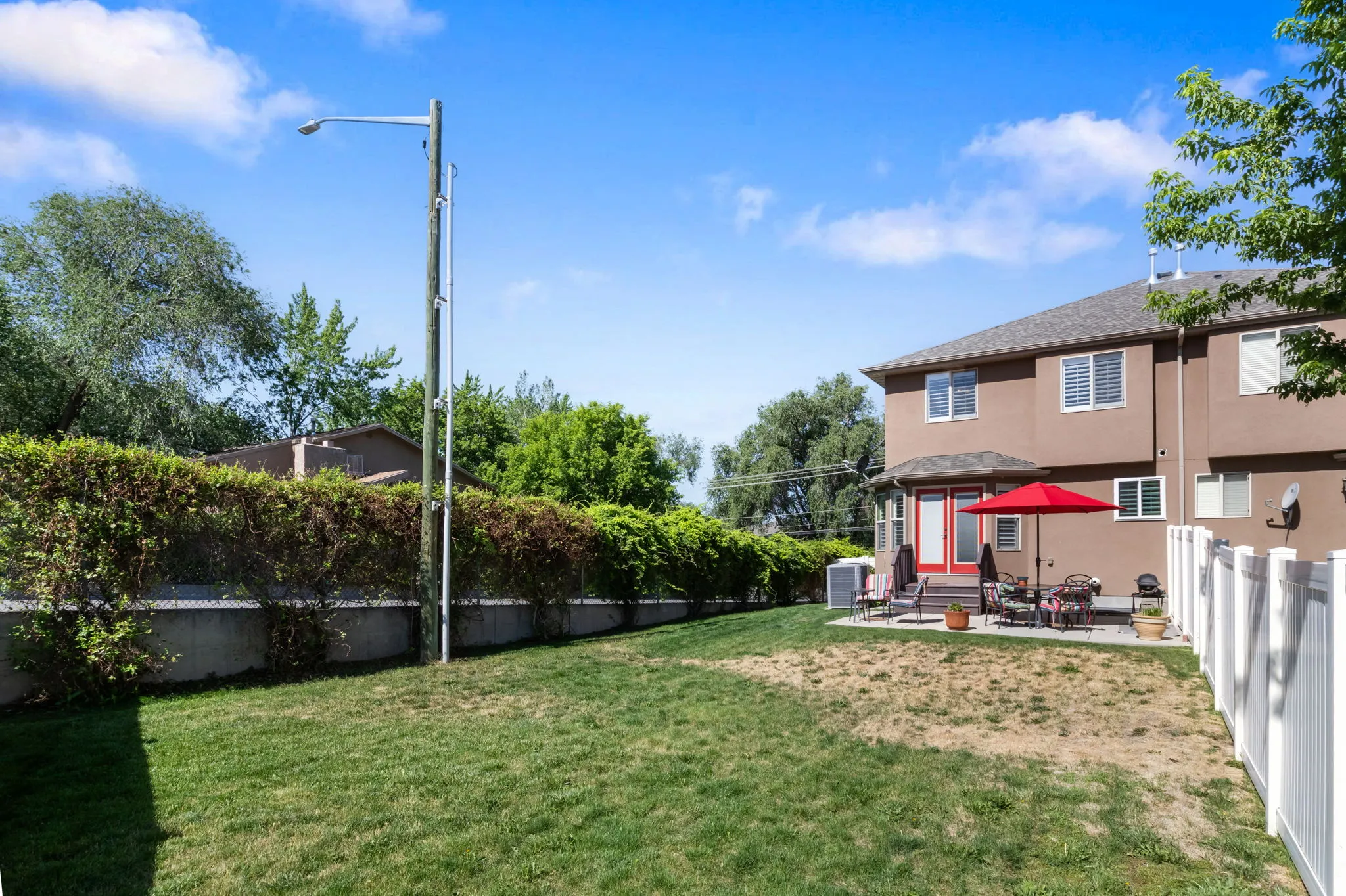 Backyard featuring a concrete patio, white privacy fence, and mature perimeter hedging
