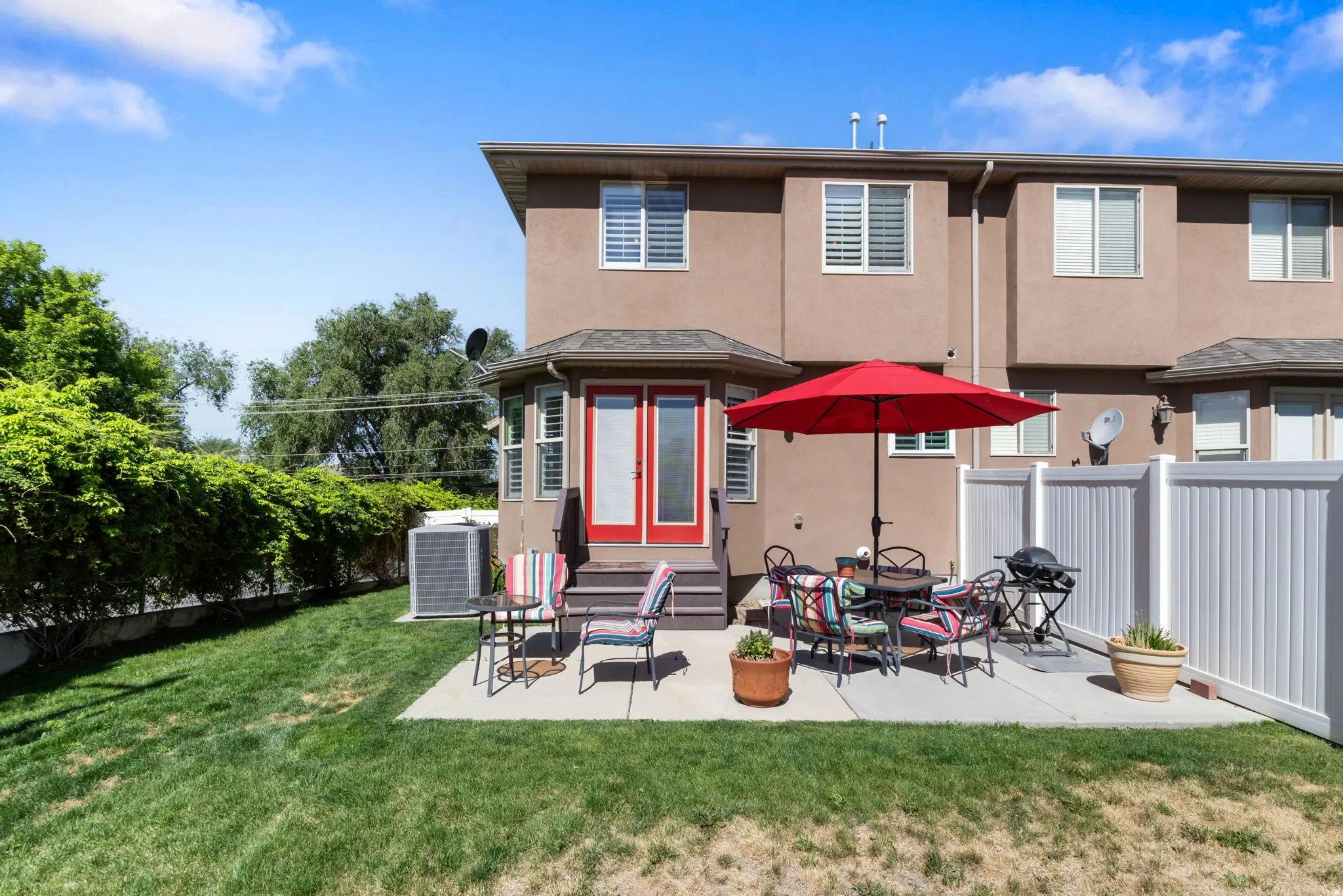 Rear exterior featuring a concrete patio, red French doors, and a green lawn