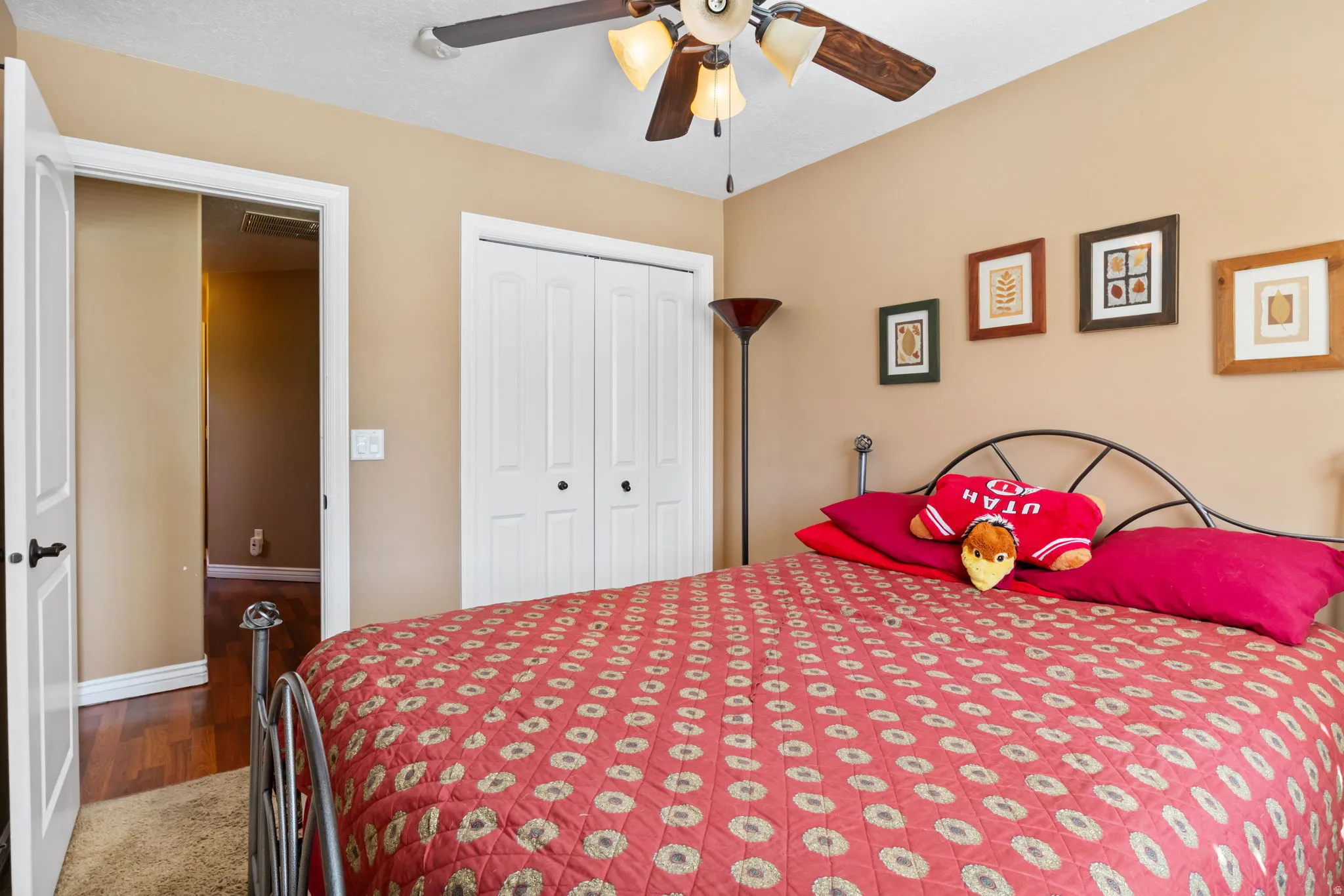 Neutral-toned room featuring a ceiling fan with integrated lighting, bi-fold closet doors, and wood-finish flooring visible through an open doorway