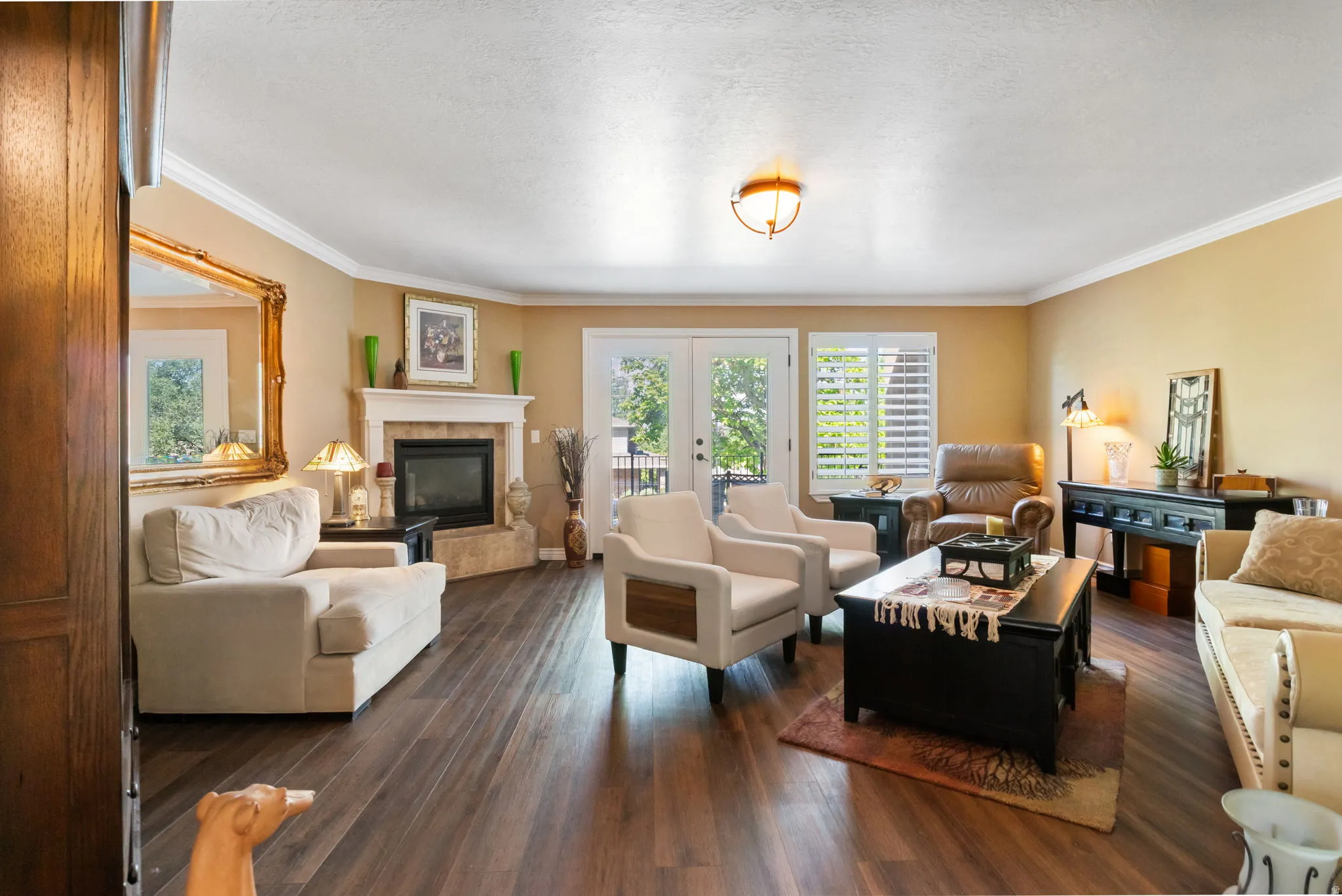 Spacious living area featuring wood-finish flooring, a corner fireplace with stone surround and mantle, and white crown molding