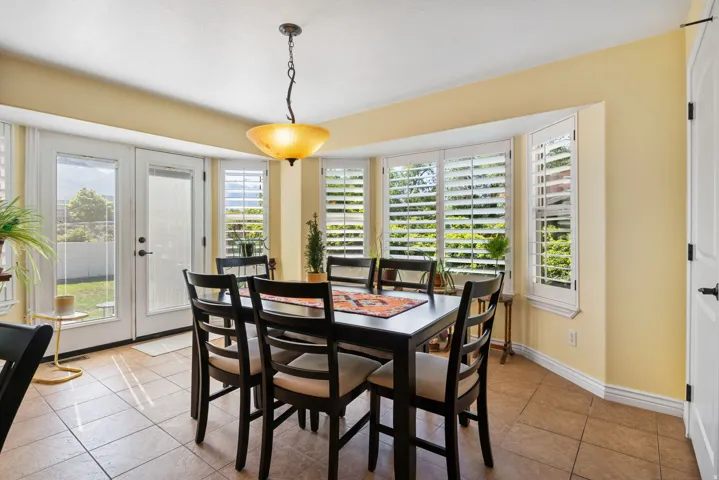 Dining area featuring tiled flooring, a bay window with plantation shutters, and a suspended ceiling light fixture
