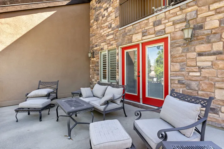Outdoor patio featuring a stone veneer wall, stucco siding, and red-framed glass doors