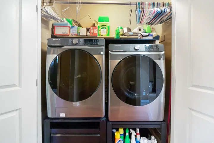 Dedicated laundry closet featuring a stainless steel front-load washer and dryer set, white bi-fold doors, and an upper storage shelf
