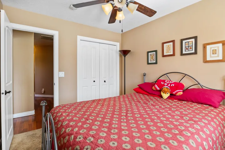 Neutral-toned room featuring a ceiling fan with integrated lighting, bi-fold closet doors, and wood-finish flooring visible through an open doorway