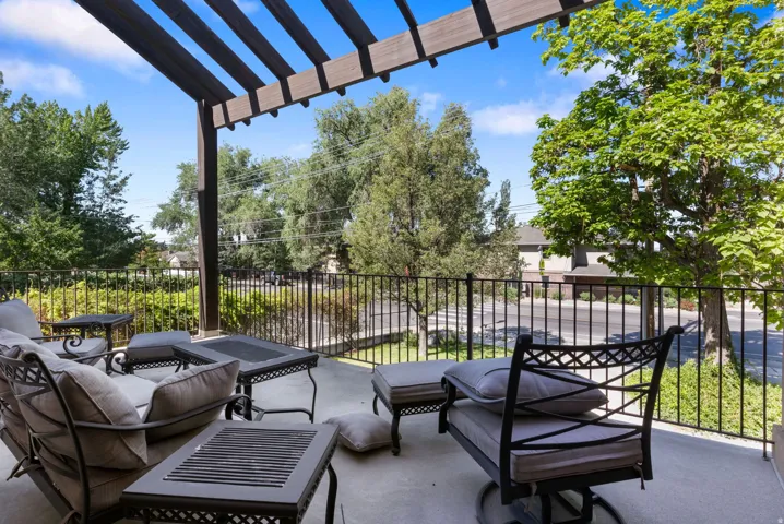 Spacious outdoor patio featuring a slatted pergola, concrete flooring, and black metal railings, surrounded by mature trees