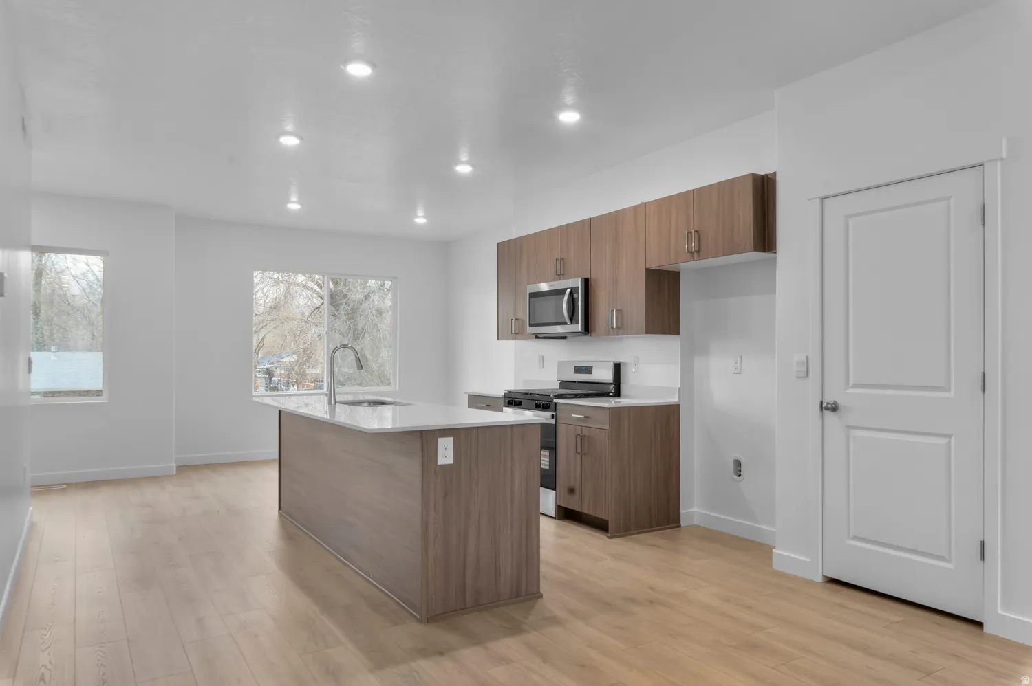 Open-concept kitchen and living area featuring wood-finish flooring, recessed lighting, and a kitchen island with a light-toned countertop and integrated sink