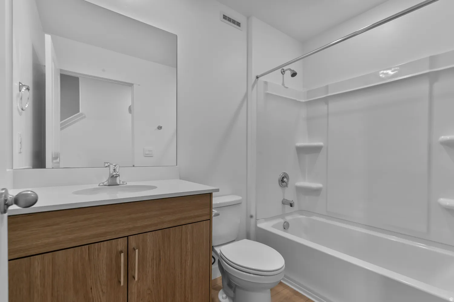 Full bathroom featuring a wood-finish vanity with a white countertop and rectangular sink, a large wall-mounted mirror, and a combined tub and shower unit with an integrated white surround