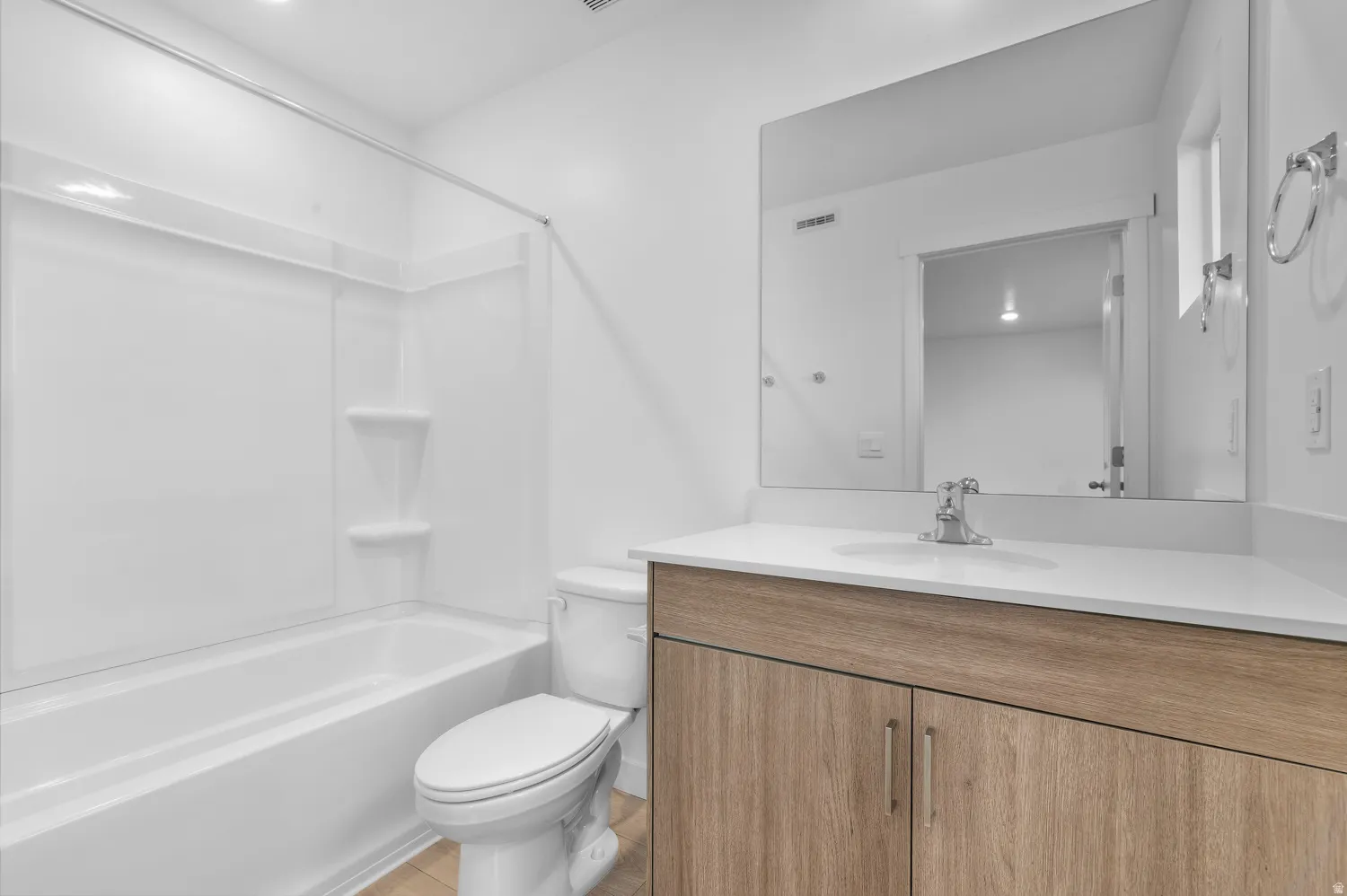 Bathroom vanity featuring a light wood-finish cabinet with silver hardware, an integrated sink, and a white countertop