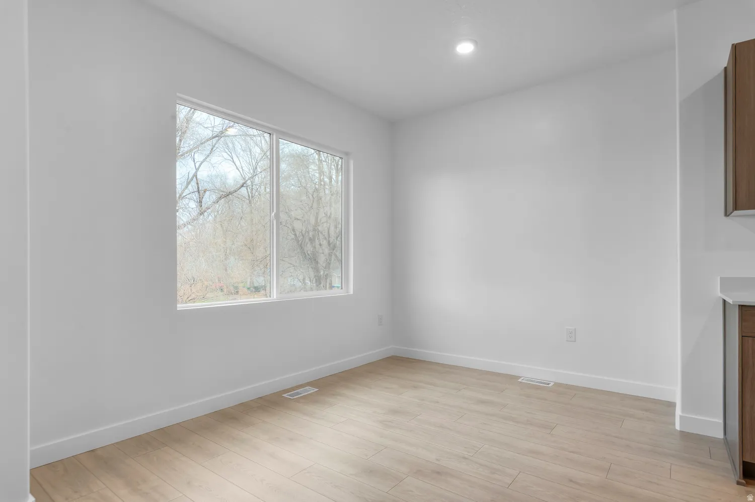 Bright interior space featuring a large window with white framing, wood-finish flooring, recessed lighting, and white baseboards