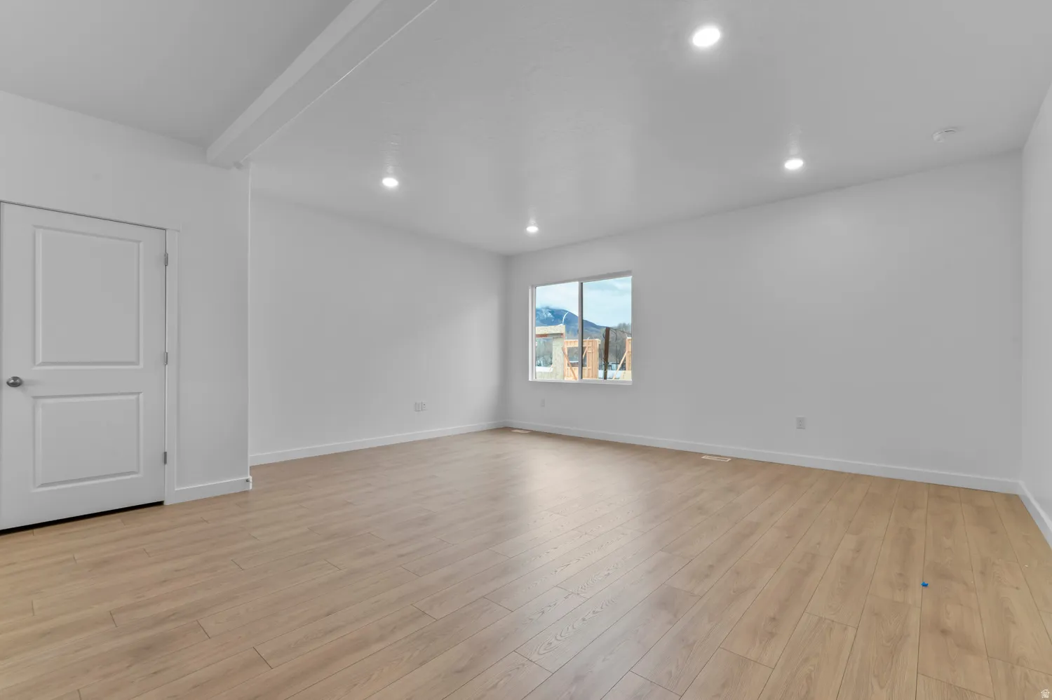 Spacious interior room featuring light wood-finish flooring, recessed lighting, white walls, white trim, and a window offering a mountain backdrop