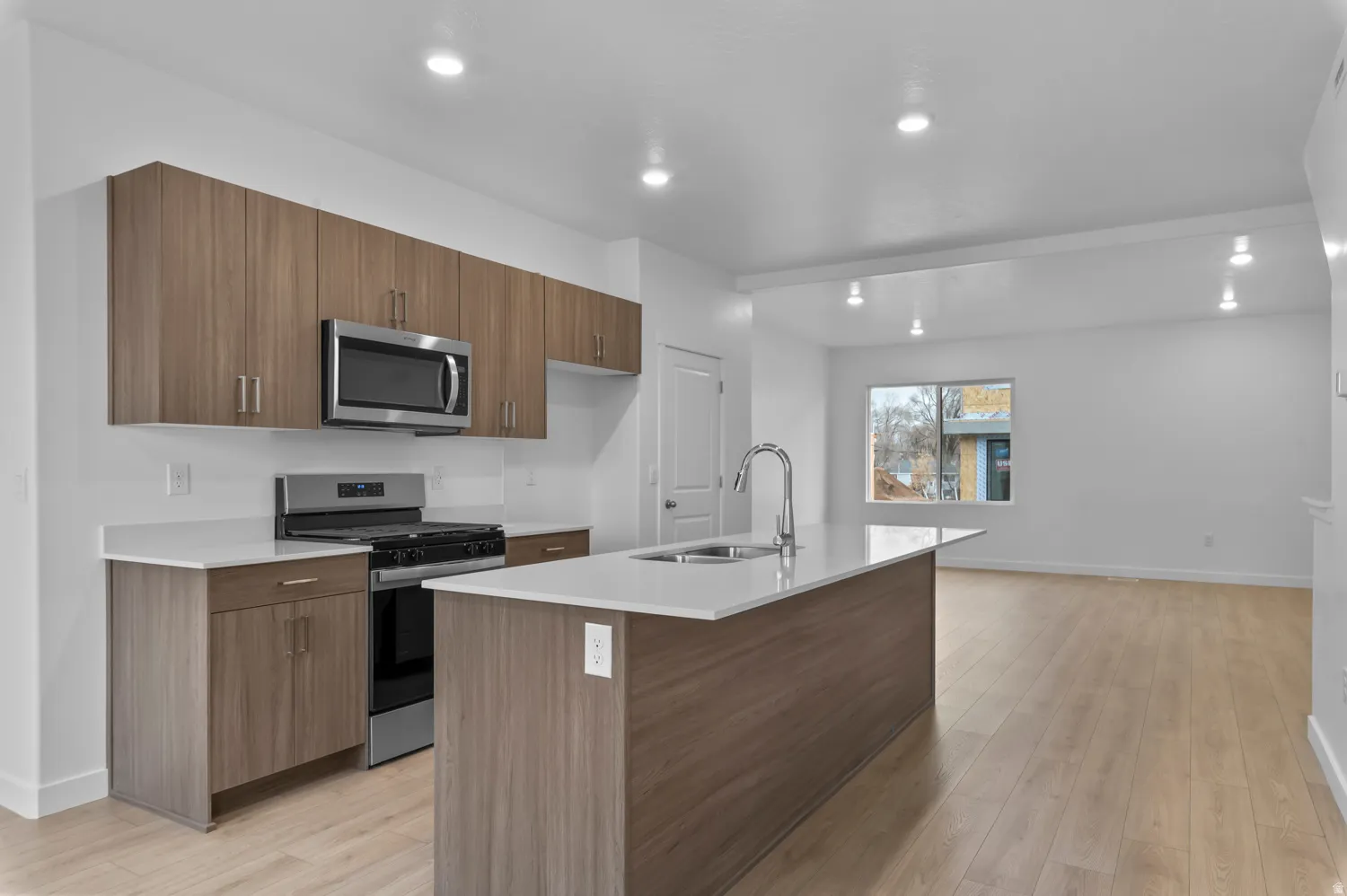 Modern kitchen featuring wood-grain cabinetry, stainless steel appliances, and light-tone countertops