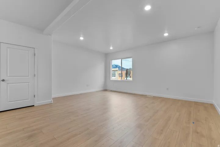 Spacious interior room featuring light wood-finish flooring, recessed lighting, white walls, white trim, and a window offering a mountain backdrop