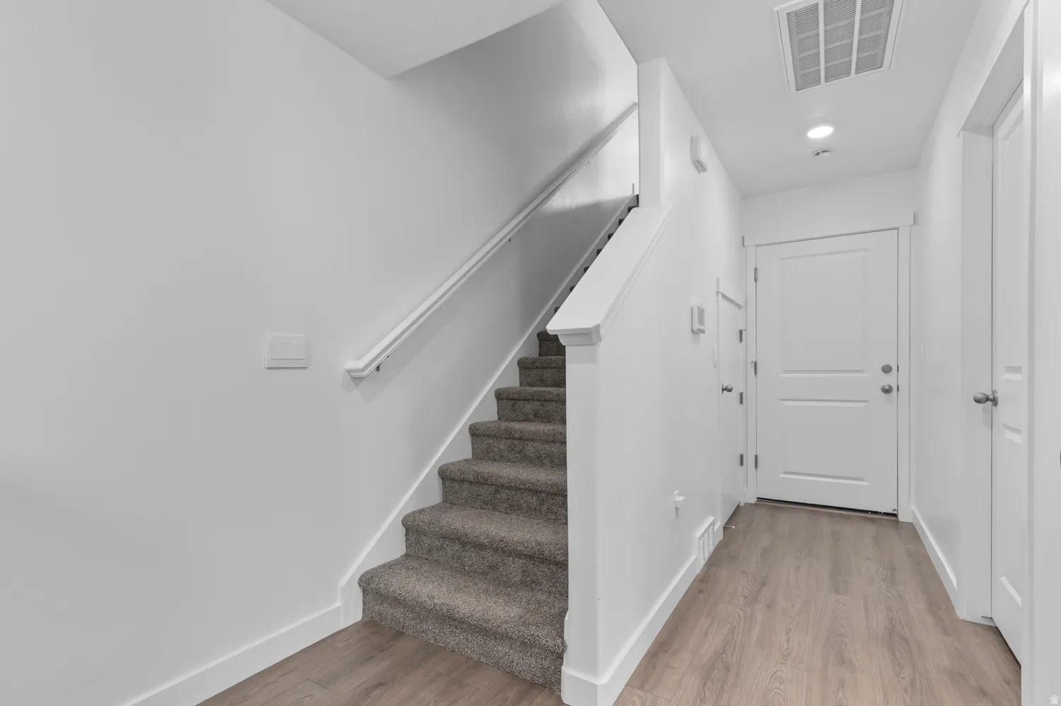 Foyer featuring wood-finish flooring and a carpeted staircase with a white handrail