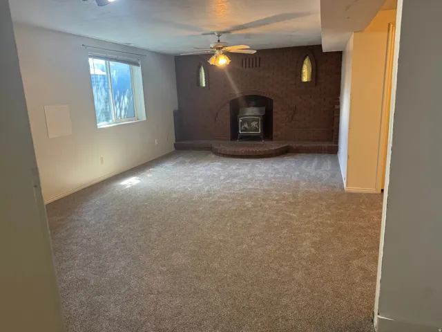 Spacious room featuring a brick fireplace with a wood-burning stove insert, a built-in hearth, and new neutral-toned carpet