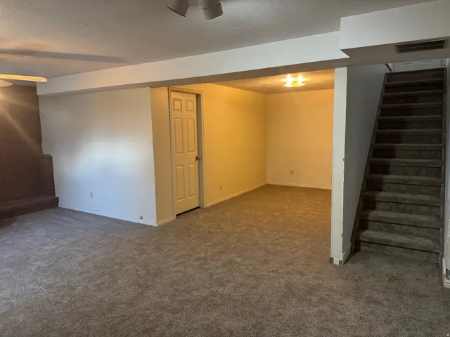 Carpeted lower-level room featuring a brick fireplace surround, a closed interior door, and a carpeted staircase