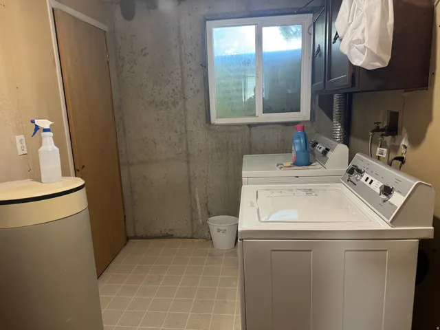 Dedicated utility space featuring concrete walls, a light-toned vinyl tile floor, a window providing natural light, and a built-in dark wood cabinet
