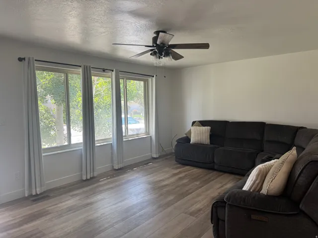 Living space featuring wood-finish flooring, a ceiling fan with integrated lighting, and multiple windows