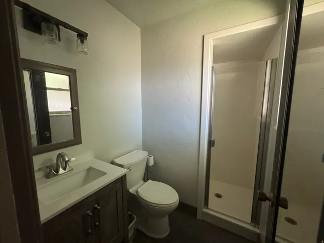 Full bathroom featuring a walk-in shower with glass enclosure, white vanity countertop, wood-finish vanity with drawer pulls, brushed nickel faucet, and a wall-mounted medicine cabinet with a mirror