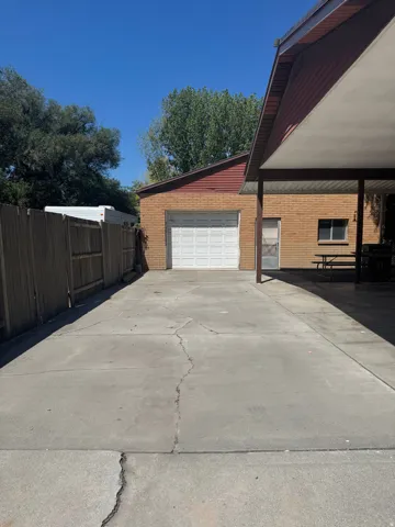 Concrete driveway with wooden fencing, brick garage with white garage door, and covered carport