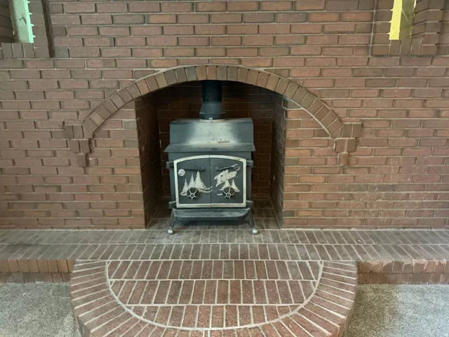 Brick fireplace with an arched opening housing a black wood-burning stove