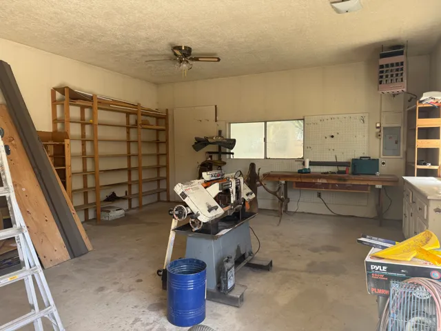 Spacious utility room featuring a concrete floor, built-in wooden shelving, two windows, a ceiling fan, and wall-mounted electrical panels