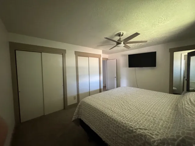 Interior room featuring two sliding door closets with wood-finish trim, a ceiling fan with integrated lighting, and carpet flooring