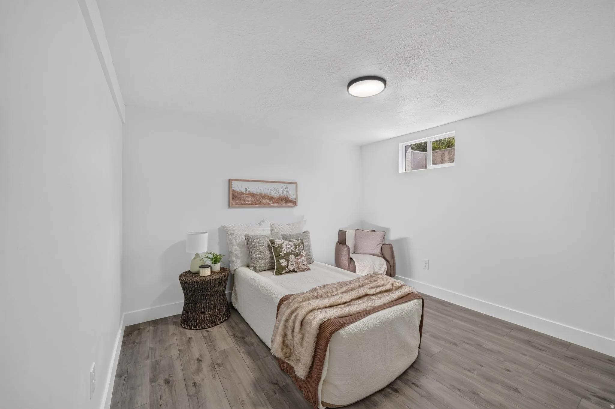 Bedroom with wood-finish flooring, white baseboards, and a window