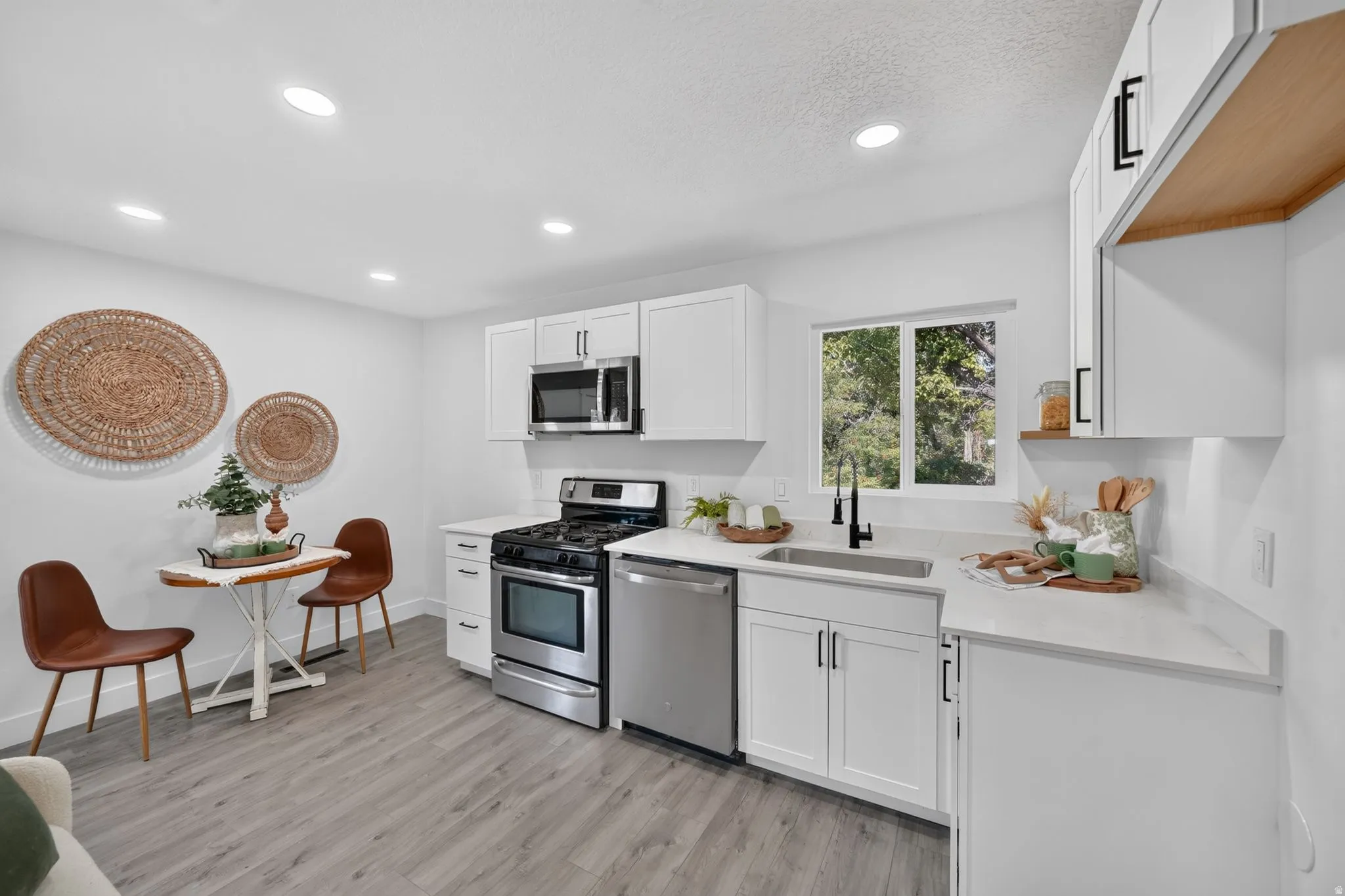 Kitchen featuring white cabinetry with black hardware, stainless steel appliances, light gray wood-finish flooring, recessed lighting, and a window above the sink
