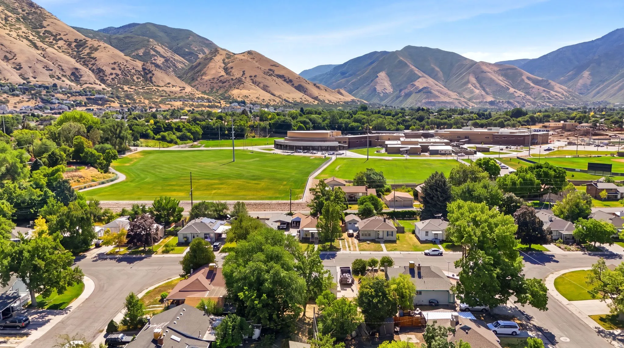 Expansive neighborhood featuring mature trees, residential properties, paved streets with curb appeal, and distant mountainous terrain
