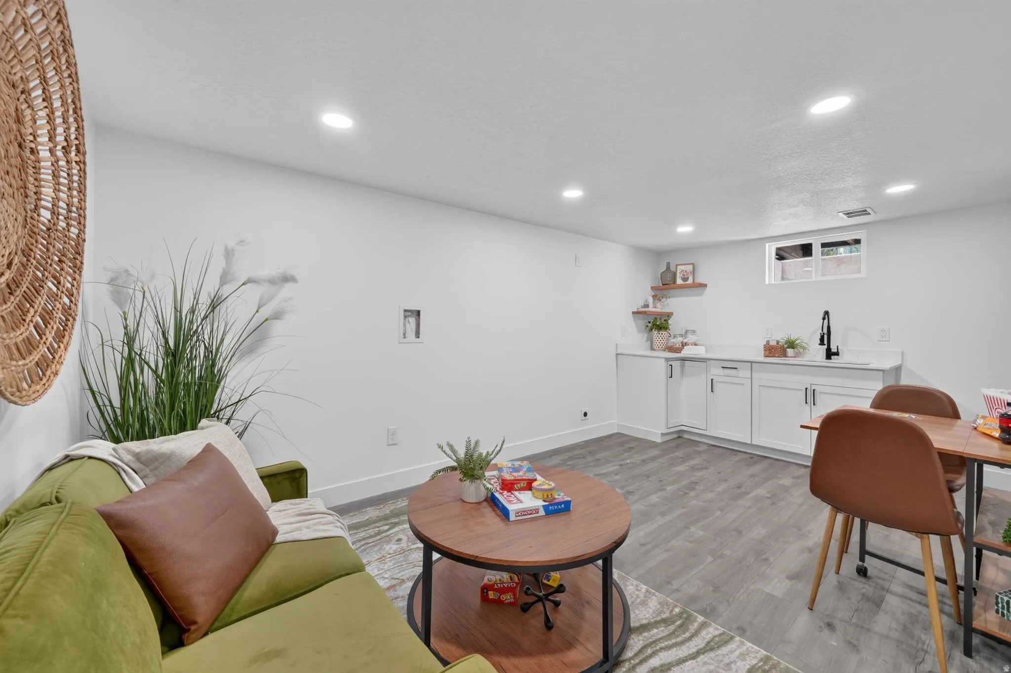 Finished basement space featuring wood-finish flooring, recessed lighting, and a kitchenette white cabinetry and a black faucet