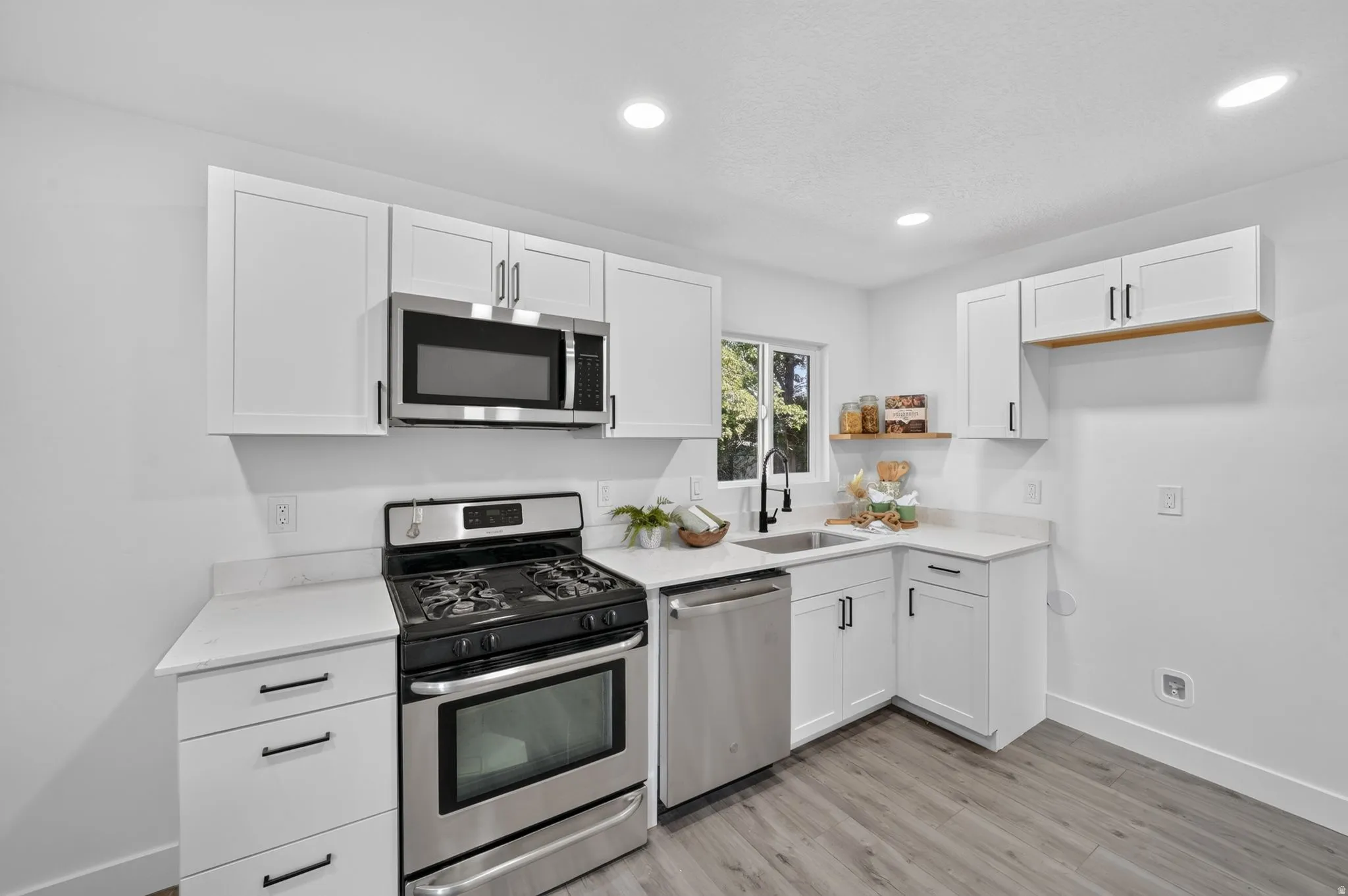 Modern kitchen featuring white cabinetry with matte black hardware, stainless steel appliances, and light countertops
