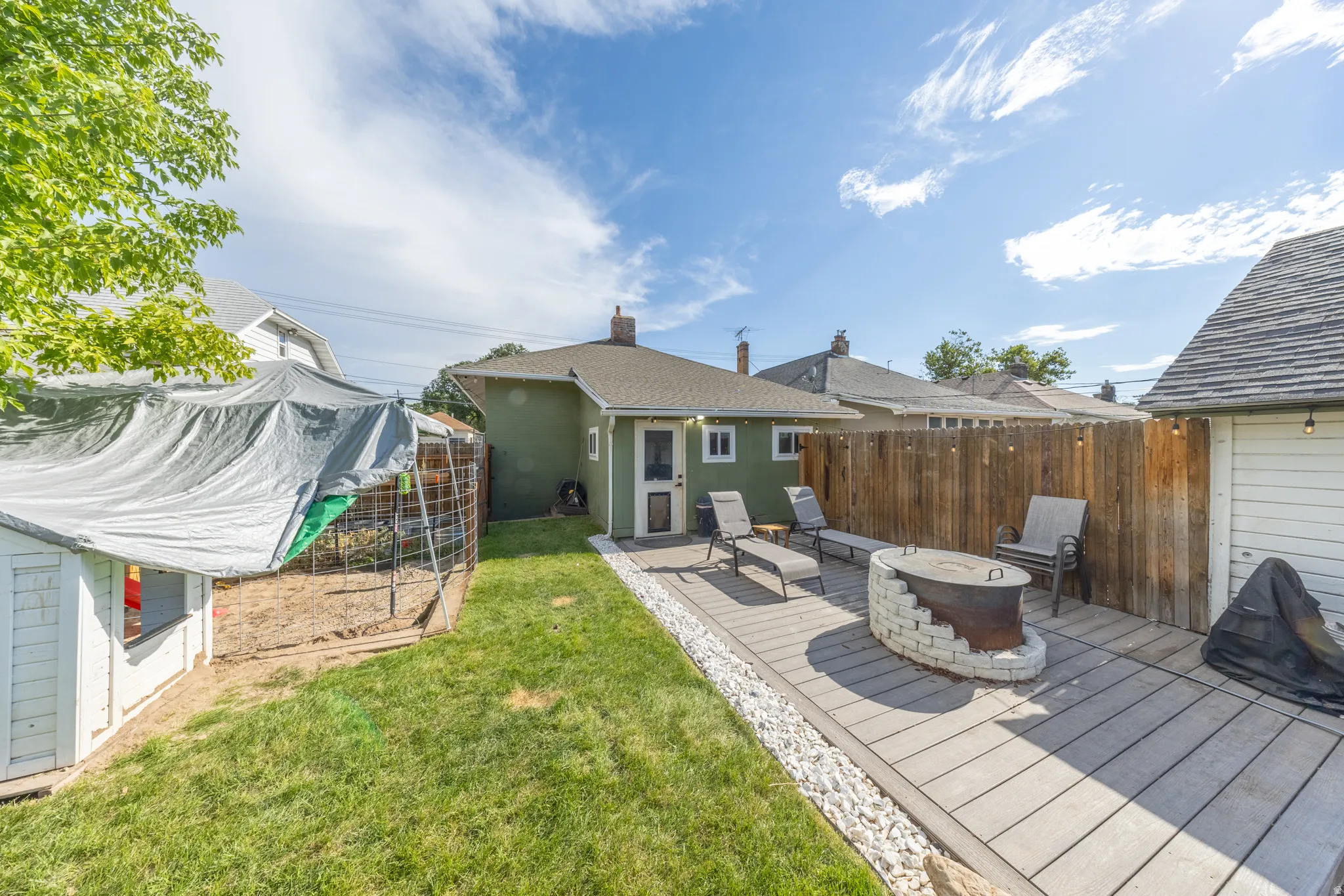Expansive backyard featuring a wood-finish deck with a stone fire pit, bordered by white gravel