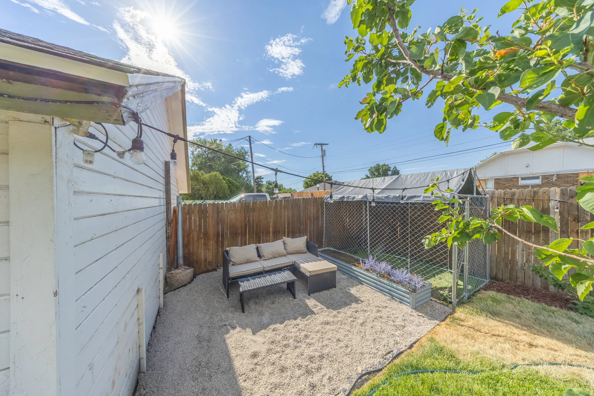 Gravel patio area featuring string lighting, wood plank siding, a wood fence, and a galvanized steel planter box