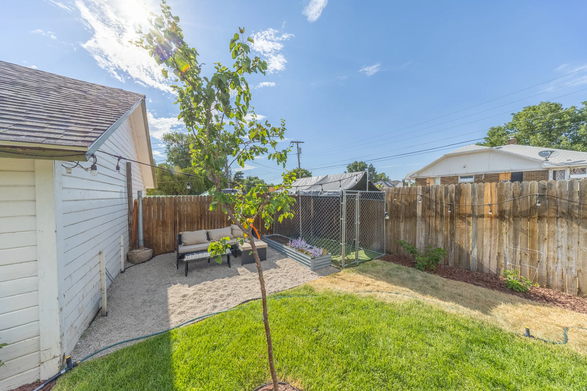 Expansive backyard featuring a gravel patio area, a manicured lawn, a chain-link enclosure, and a wood privacy fence