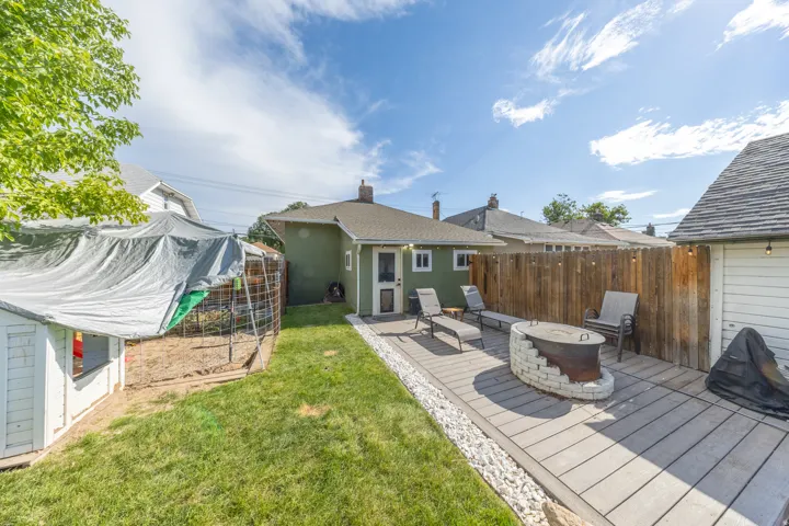 Expansive backyard featuring a wood-finish deck with a stone fire pit, bordered by white gravel