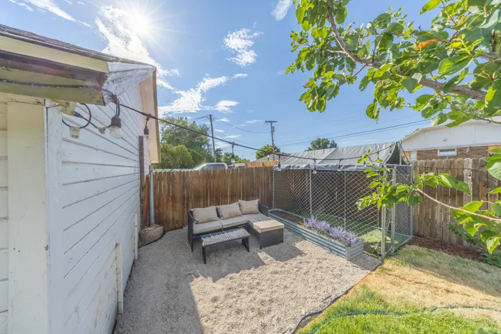 Gravel patio area featuring string lighting, wood plank siding, a wood fence, and a galvanized steel planter box