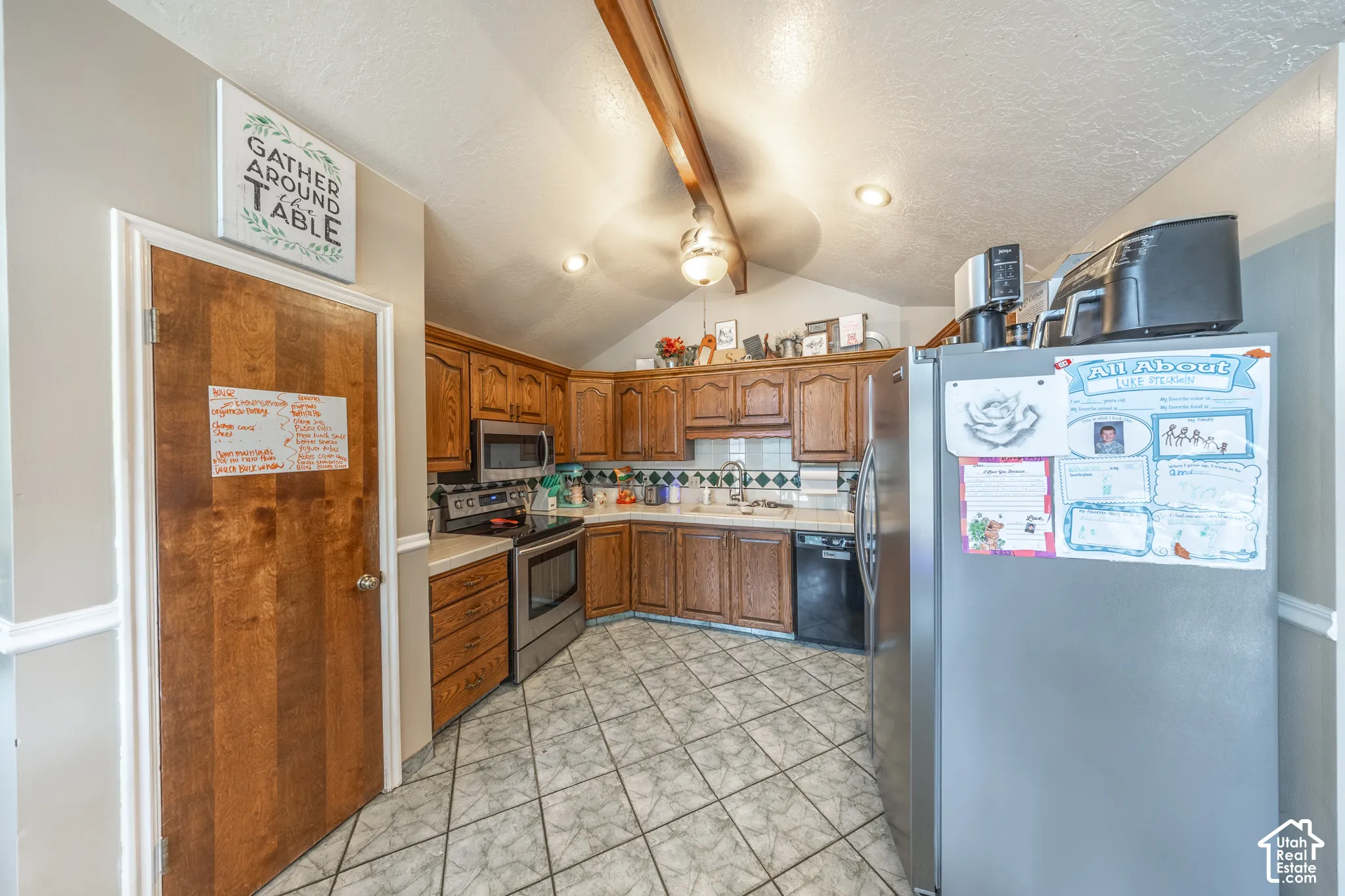Kitchen featuring wood cabinetry, stainless steel appliances, white patterned tile flooring, and a vaulted ceiling with exposed wood beams