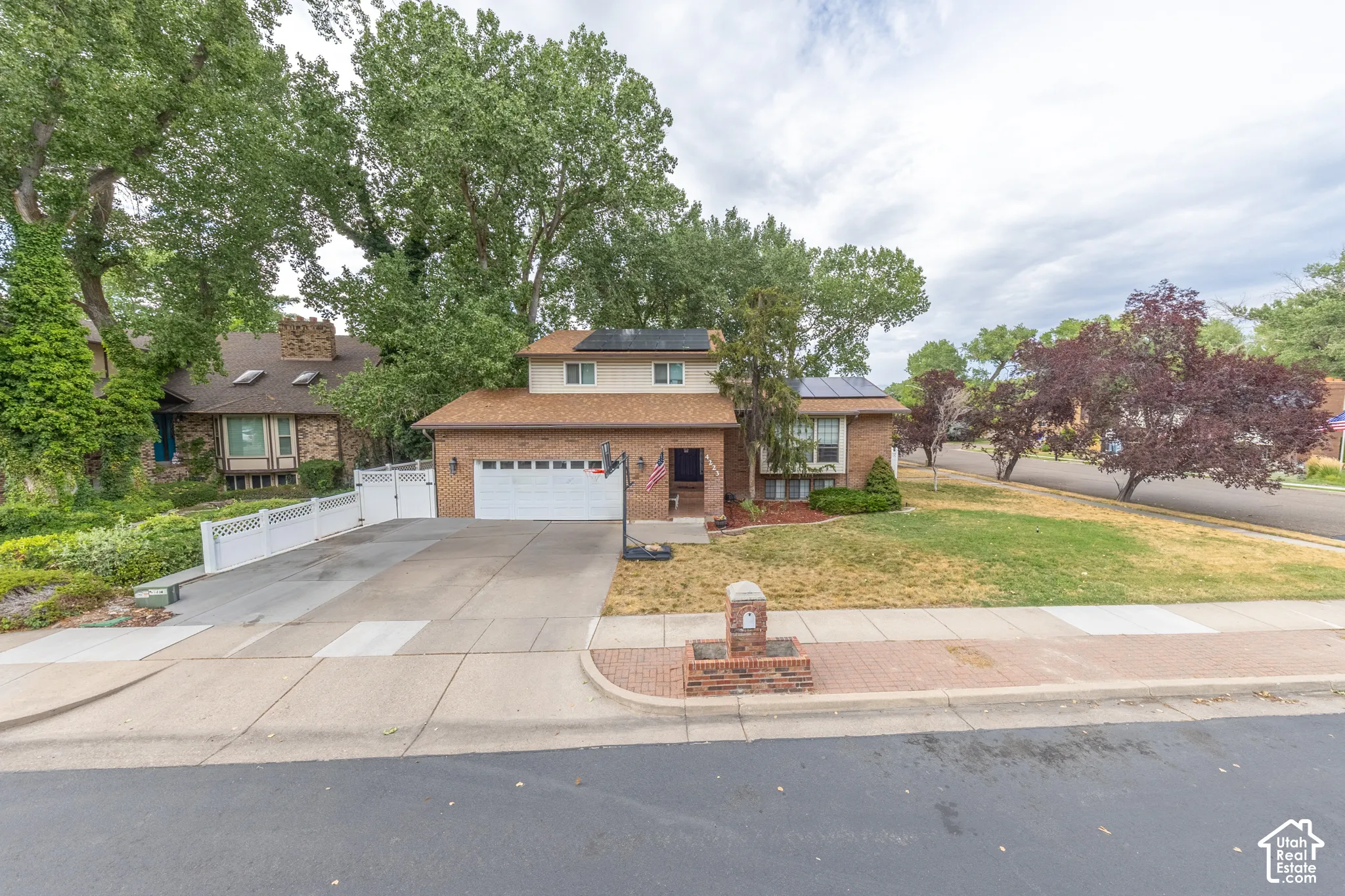 Brick exterior featuring a two-car garage, solar panels, a concrete driveway, and mature landscaping