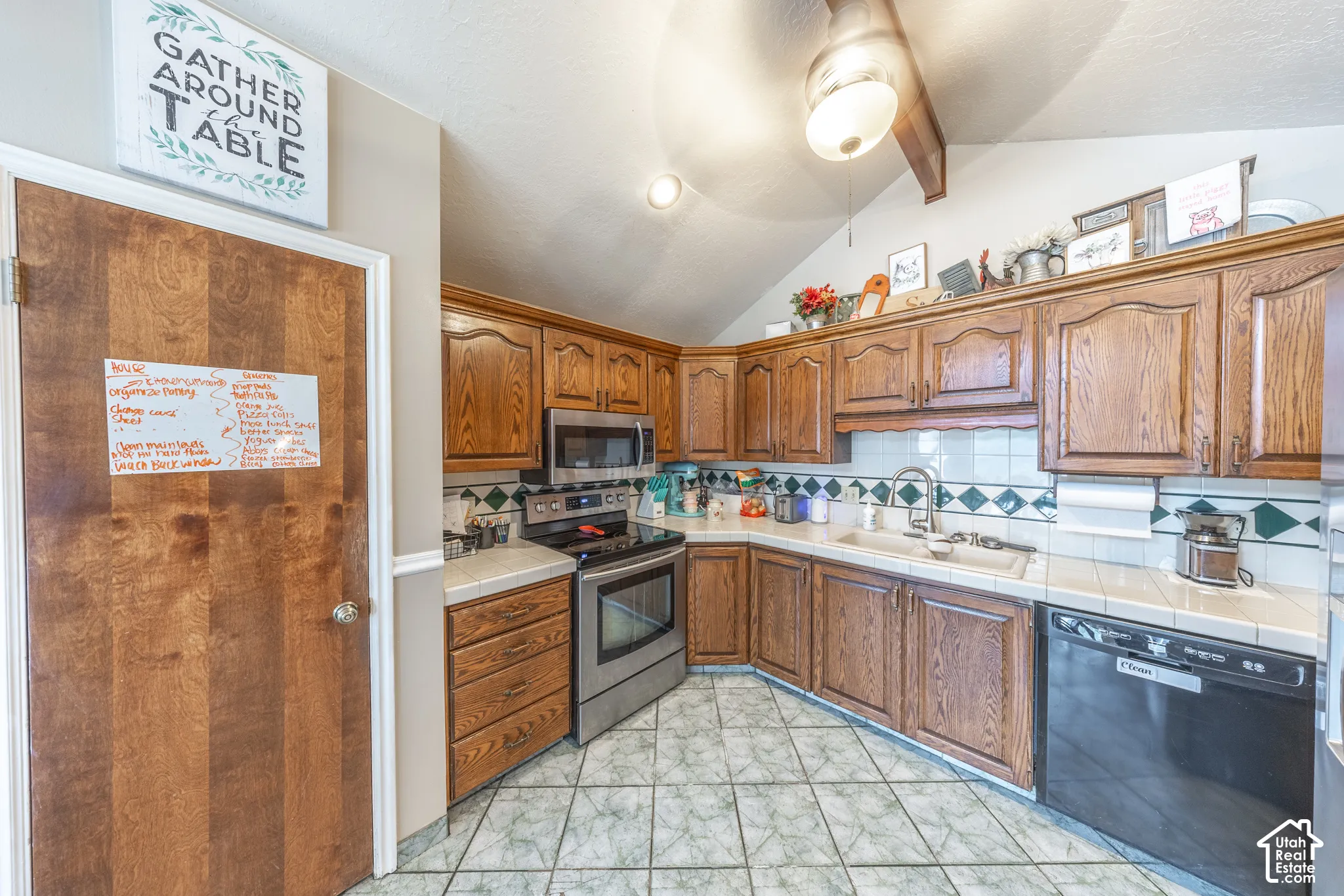 Kitchen featuring wood-finish cabinetry, stainless steel appliances, tiled countertops, and a patterned tile backsplash