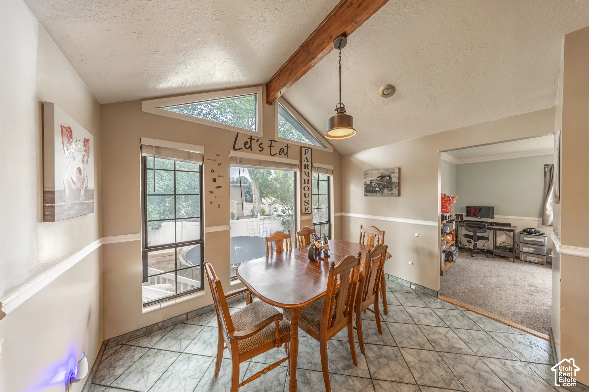 Dining area featuring a vaulted ceiling with exposed wood beam, large windows including triangular transoms, and tile flooring