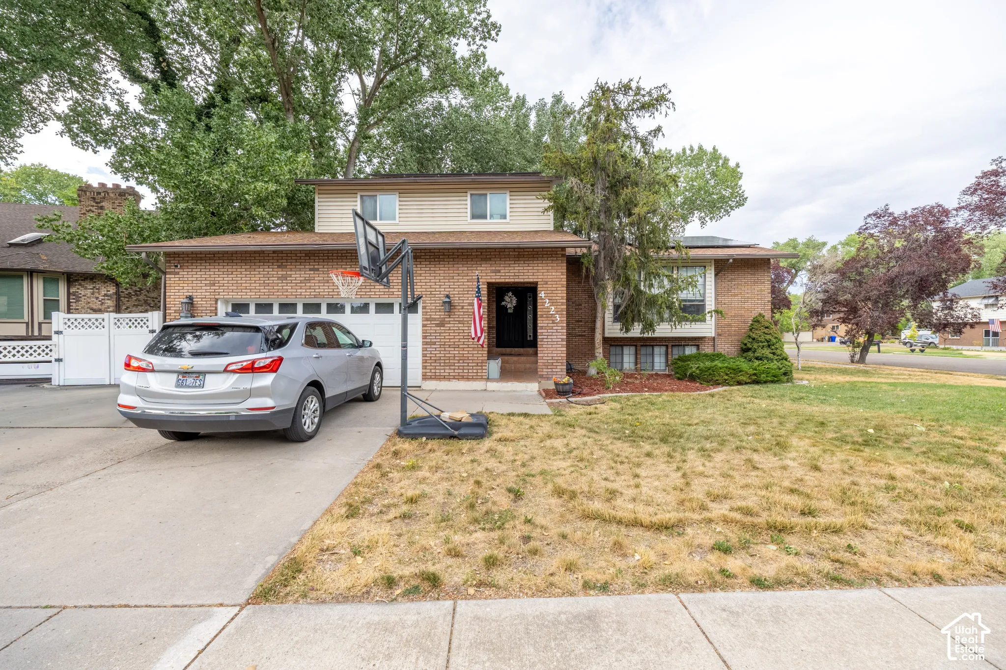 Brick and siding exterior featuring an attached garage, paved driveway, mature trees, and established landscaping