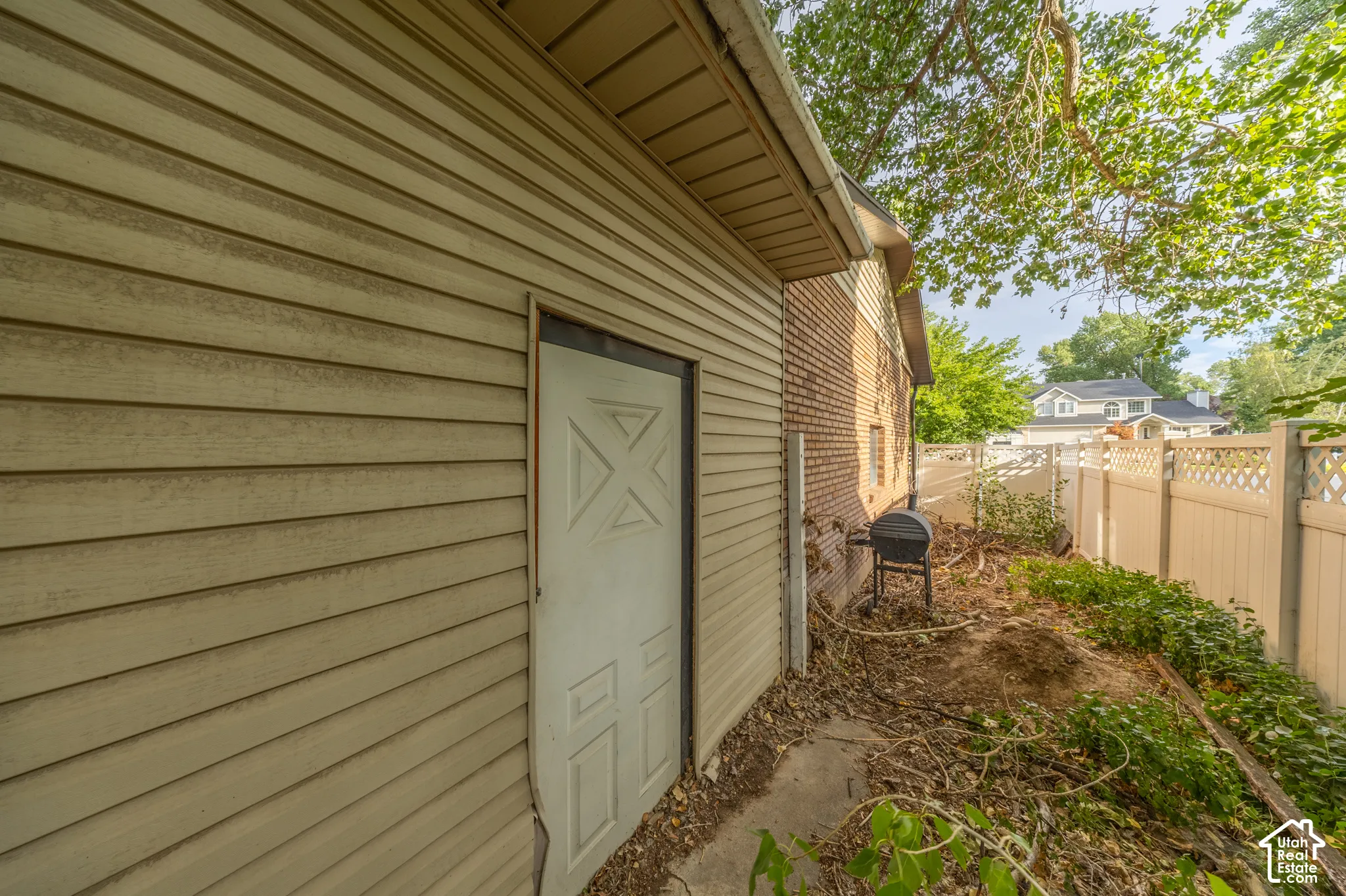 Exterior featuring horizontal panel siding, a white service door, and a lattice-top privacy fence