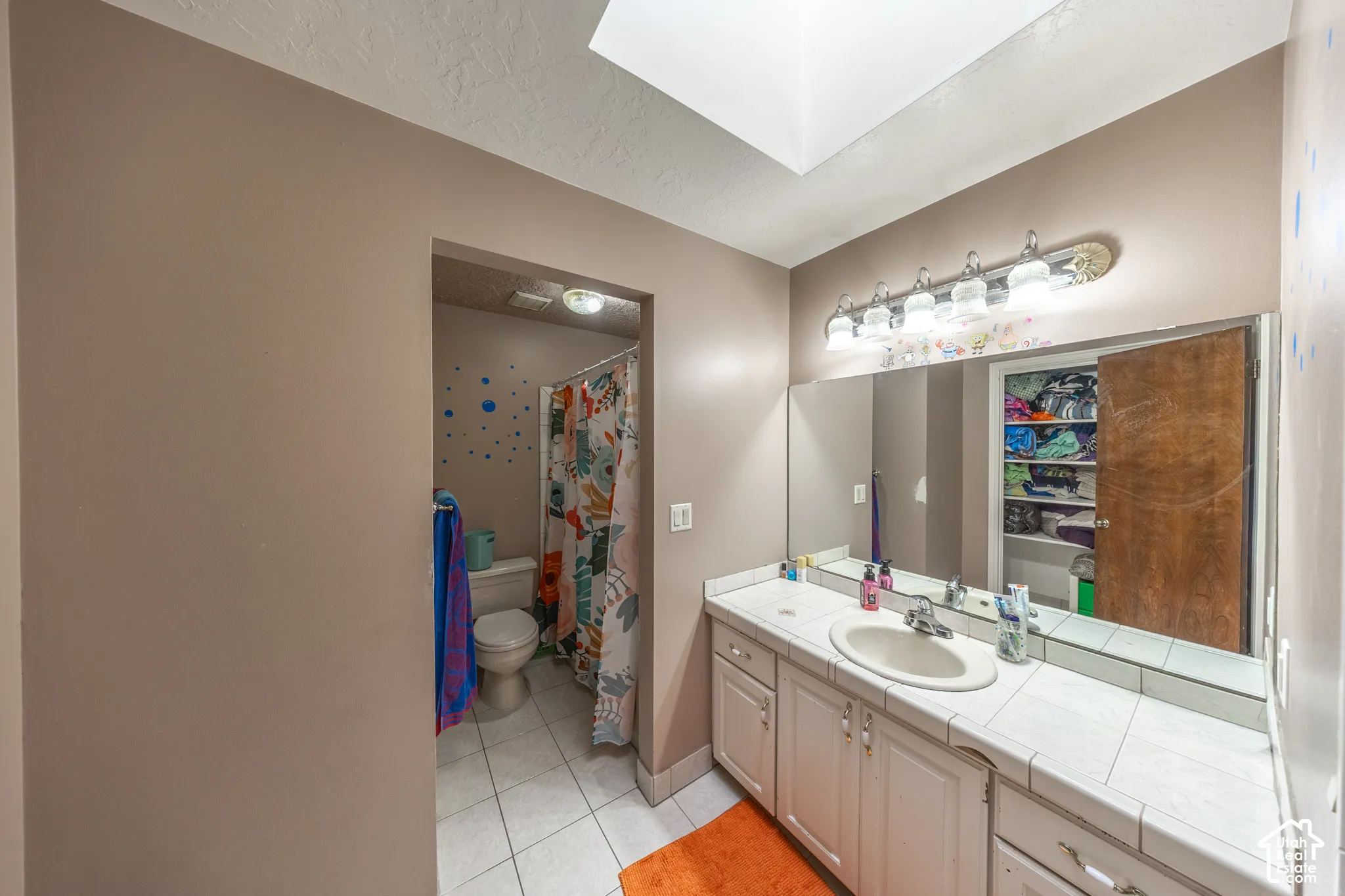 Bathroom featuring a single vanity with a white tile countertop, an undermount sink, a large wall-mounted mirror, and a five-light vanity fixture