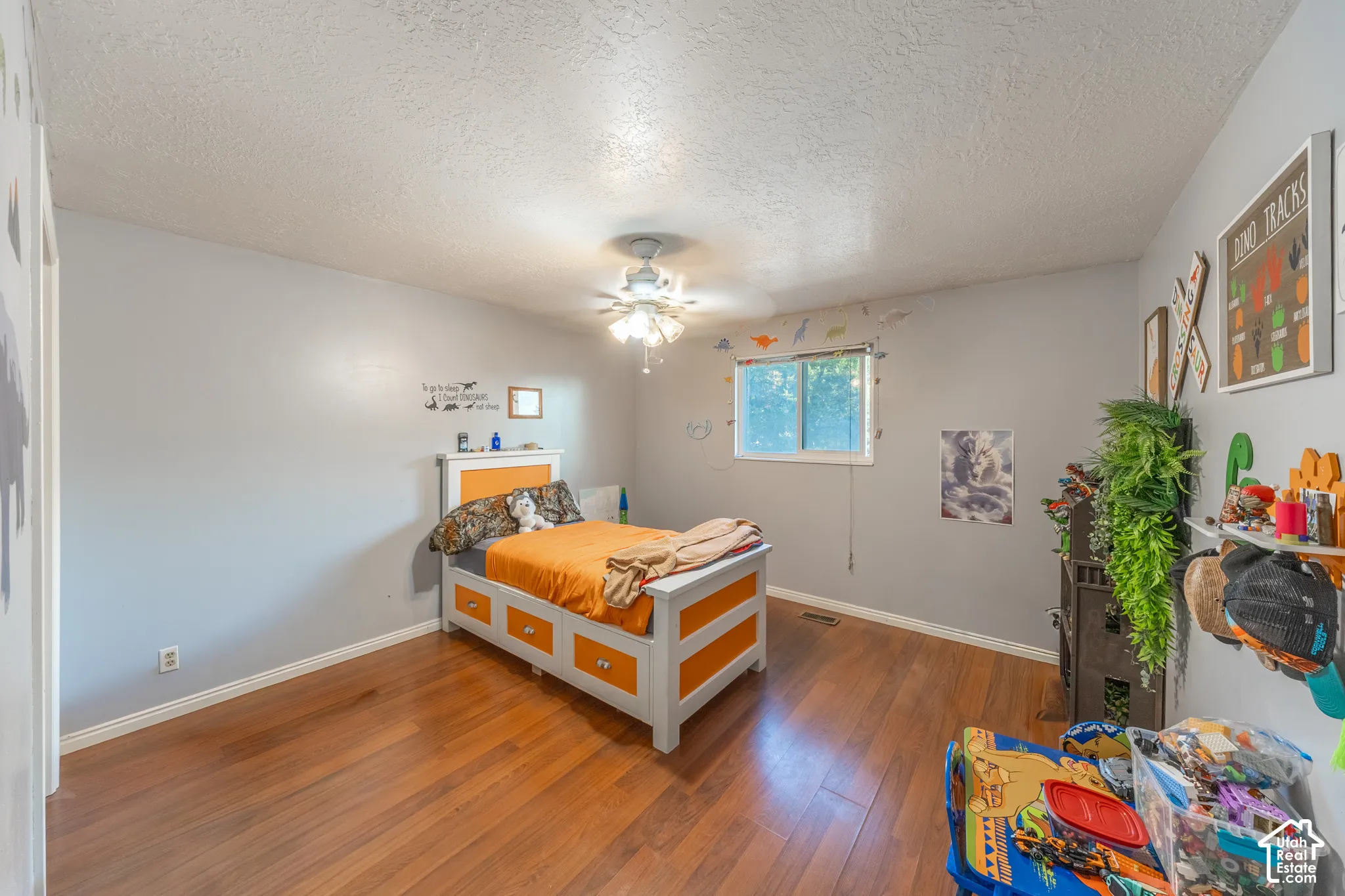 Wood-finish flooring with light gray walls, a textured ceiling, and a ceiling fan with integrated lighting