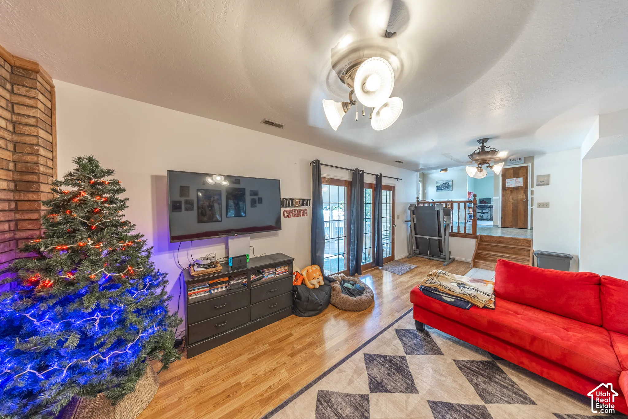 Living area featuring wood-finish flooring, a brick fireplace surround, and multiple ceiling fans