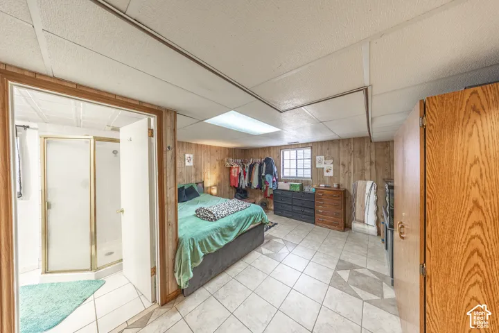 Spacious room with wood paneling, tile flooring, a window, recessed ceiling lighting, and an adjacent bathroom featuring a glass-enclosed shower