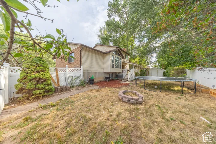 Spacious backyard featuring a stone fire pit, tiered landscaping, and a white privacy fence
